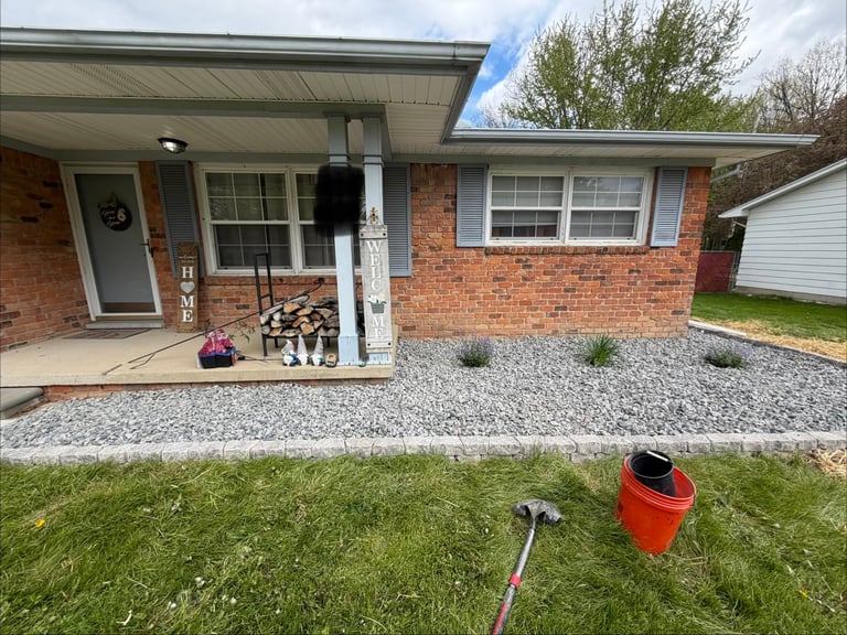 Front exterior of a single-story red brick house with white trim, gravel landscaping, and green lawn
